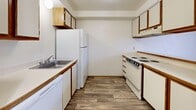 This single-floor residence offers a practical and comfortable layout with a clean, neutral aesthetic throughout. The interior is characterized by crisp white walls, wood-trimmed doors and accents, and a combination of durable hardwood-style flooring and plush carpet, creating a warm and functional living environment.

The kitchen is designed for efficiency, featuring a galley-style layout with white cabinetry trimmed in wood, ample counter space, a stainless steel sink, and white appliances including a refrigerator, electric range, and dishwasher. Wood-look flooring adds a welcoming touch to this practical cooking space.

The living and dining areas benefit from wood-style flooring and generous windows fitted with blinds, allowing natural light to brighten the rooms while offering views of the surroundings. A ceiling fan with a light fixture provides added comfort and ventilation to one of the main living areas.

The bedrooms are carpeted for comfort and offer closet storage, with one room featuring a window that invites natural light. A hallway with wood-style flooring connects the rooms seamlessly, with interior doors featuring warm wood-toned finishes.

The bathroom is well-appointed with a full soaking tub and shower combo, a vanity with storage drawers, a mirror, and wood-look flooring that ties in with the rest of the home's design. The overall ambiance is bright, clean, and move-in ready.