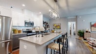 Located at 9100 S 59th Ave in Phoenix, AZ, this well-appointed single-story home offers 2 bedrooms and 2 bathrooms across a smartly utilized floor plan. The heart of the home is an open-concept kitchen, dining, and living area that creates a seamless flow for everyday living and entertaining. The kitchen stands out with crisp white upper cabinetry, contrasting dark lower cabinets, a striking geometric tile backsplash, stainless steel appliances, and a large center island with a quartz countertop and bar seating beneath a modern geometric pendant light. Wood-look flooring runs throughout, adding warmth and continuity. The living room offers a cozy yet functional space with recessed lighting and direct access to a private covered patio, perfect for outdoor dining with views of surrounding greenery. The primary bedroom is generously sized, featuring multiple windows that invite natural light, a ceiling fan, and access to a walk-in closet. The bathrooms are finished with quartz countertops, undermount sinks, gray cabinetry with brushed metal hardware, and large mirrors. A hallway connects the private quarters seamlessly to the main living areas, completing this thoughtfully designed home.