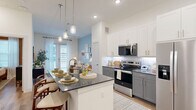 Located at 8100 Brewer Blvd in Fort Worth, TX, this one-bedroom, one-bathroom residence offers a well-designed single-floor layout. The open-concept living area seamlessly connects the kitchen, dining, and living spaces, creating an efficient and inviting atmosphere. The kitchen is appointed with two-tone cabinetry — crisp white uppers paired with grey lowers — granite countertops, a tile backsplash, stainless steel appliances including a side-by-side refrigerator, electric range, and built-in microwave, as well as a peninsula with seating that doubles as a dining space. Pendant lighting and recessed fixtures illuminate the area, while light hardwood-style flooring flows throughout. The living area connects to a private patio, bringing in natural light through large windows. The bedroom features warm-toned walls, ample natural light from multiple windows, and access to a walk-in closet with built-in shelving. The bathroom is finished with matching grey cabinetry, granite countertops, and a soaking tub with a tile surround. Additional conveniences include in-unit laundry, a pantry, and two closets, rounding out this thoughtfully appointed residence.