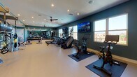 Located at 10858 Telegraph Rd in Ventura, California, this fitness and yoga center is a thoughtfully designed, single-floor facility built to support a comprehensive workout experience. The space features deep teal accent walls paired with light-toned flooring, recessed lighting, and ceiling fans that contribute to a clean, energizing atmosphere throughout.

The main workout area is generously proportioned, offering ample room for a wide range of cardio and strength training equipment. Cardio options include treadmills with individual monitors, elliptical trainers, stair climbers, rowing machines, and stationary cycling bikes. A multi-function cable resistance machine provides versatility for full-body strength training, while a dedicated dumbbell rack lines one side of the room for free weight exercises.

Full-length mirrors run along one wall, enhancing the sense of openness and allowing users to monitor their form during workouts. Multiple flat-screen TVs are mounted along the teal walls, providing entertainment and additional motivation. Large windows along the exterior wall invite natural light and offer views of the surrounding Ventura neighborhood.

A dedicated yoga and flexibility area is accessible via glass-paneled sliding doors, stocked with stability balls, resistance tools, and mats. This separation allows for quieter, low-impact training alongside the main fitness floor, making the facility suitable for a broad range of fitness activities and skill levels.