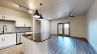 Located in Grapevine, TX, this well-appointed 1-bedroom, 1-bathroom residence offers a thoughtfully designed single-floor layout that maximizes functionality and style. The open-concept kitchen and living area serves as the heart of the home, anchored by a striking curved granite-topped island illuminated by dual pendant lights and a track lighting system. The kitchen is outfitted with crisp white cabinetry featuring black hardware, a herringbone tile backsplash, dark granite countertops, and a full suite of stainless steel appliances including a French door refrigerator, range, microwave, and dishwasher. Hardwood-style flooring flows throughout the main living areas, complemented by a ceiling fan and French doors that open to an outdoor area, allowing natural light to fill the space. The bedroom is carpeted and comfortably sized, featuring a window with blinds and access to two closets. The bathroom mirrors the kitchen's design aesthetic with white cabinetry, dark granite counters, a large vanity mirror, and a glass-enclosed shower. A dedicated in-unit laundry area accommodates a full-size washer and dryer. A hallway connects all rooms efficiently, completing this clean and modern layout.