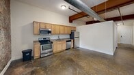 Located at 2001 E Franklin St in Richmond, Virginia, this one-bedroom, one-bathroom loft blends industrial character with functional design across a single floor. The open-plan living and kitchen area immediately impresses with its exposed brick accent wall, polished concrete floors, and prominent overhead ductwork — hallmarks of classic loft-style architecture. Natural light filters in through tall windows fitted with blinds, offering views of the surrounding streetscape.

The kitchen is thoughtfully equipped with light maple cabinetry, granite-style countertops, and a full suite of stainless steel appliances, including a range, microwave, dishwasher, and refrigerator. Exposed wooden beams overhead add warmth and contrast to the industrial elements.

The bedroom features the same concrete flooring and a ceiling fan, with a high transom window that allows light in while maintaining privacy. A dedicated utility area houses a stacked washer and dryer alongside additional closet storage, adding everyday convenience.

The bathroom is finished with floor-to-ceiling neutral tile, a mosaic accent border, and a full tub-shower combination — providing a clean, classic aesthetic. The overall ambiance of this space is distinctly urban, offering an authentic loft experience in the heart of Richmond.
