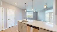 This well-appointed single-floor residence showcases a thoughtful open-concept layout that seamlessly connects the kitchen, dining, and living areas. The kitchen is a standout feature, equipped with stainless steel appliances including a range, microwave, dishwasher, and refrigerator. Gray shaker-style cabinetry pairs elegantly with white quartz countertops, while a central island with an undermount sink and pendant lighting adds both function and style. Light wood-tone flooring runs throughout the unit, creating a warm, cohesive aesthetic.

The living and dining areas benefit from generous natural light through large windows and a set of French doors that open to an outdoor balcony, complemented by a ceiling fan and a gold chandelier fixture. A wide, clean-lined hallway connects the living spaces to the private quarters, which include well-sized bedrooms, one of which features direct access to a bathroom.

The bathroom is refined in design, featuring a dual-sink vanity with white quartz countertops, gray cabinetry, a large wall mirror, and a tiled tub-shower combination. A spacious walk-in closet with wire shelving provides ample storage. Throughout the residence, neutral gray tones, recessed lighting, and clean white trim create a modern, move-in-ready ambiance.