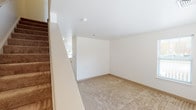 This two-floor space is designed with functionality and accessibility in mind. The layout, as revealed by the 3D model, features a central staircase with a handrail connecting both levels, providing straightforward access between floors. The stairwell opens to a well-lit landing with a panel door entry point.

Throughout the space, rooms are finished with neutral beige carpeting and crisp white walls, creating a clean, understated aesthetic. Multiple rooms on both floors feature several windows dressed with white blinds, allowing for generous natural light and outdoor views of surrounding greenery. One bright room is highlighted by a pendant light fixture, adding a focal point to the space.

The kitchen is equipped with warm oak cabinetry spanning the full perimeter, offering ample storage. White appliances, including a range, refrigerator, and dishwasher, are included, and the room features tile flooring and a stainless steel sink beneath a window.

Two bathrooms serve the space. One features a tub-shower combination with chrome fixtures, while the other is designed for accessibility, equipped with grab bars positioned near the toilet and along the walls, alongside a wide-open vanity with a large mirror and a multi-bulb light fixture above.