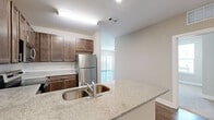 This thoughtfully designed 3-bedroom, 2-bathroom single-floor residence combines modern finishes with a practical layout across a generous footprint. The open-concept kitchen and living area serves as the heart of the home, featuring rich dark-stained cabinetry, granite-style countertops, a stainless steel appliance suite including a refrigerator, range, and microwave, and a double-basin undermount sink set into a peninsula that connects seamlessly to the living space. Wood-look plank flooring runs throughout the main living areas, adding warmth and continuity. The bedrooms are carpeted for comfort, with neutral tones throughout creating a calm, cohesive atmosphere. The primary bedroom offers a comfortable footprint and access to a dedicated closet outfitted with wire shelving systems for organized storage. Bedrooms feature large windows that invite abundant natural light and provide views of the surrounding community, including a pool and landscaped common areas. The bathrooms are finished with granite-topped dark wood vanities, undermount sinks, and wood-look flooring, with at least one bathroom featuring a walk-in shower. Clean white walls, crisp trim, and consistent finishes give the entire residence a polished, move-in-ready feel.