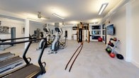 Located along I-25 N in Englewood, Colorado, this well-appointed fitness center offers a comprehensive workout environment across a single open floor. The space is bathed in bright, even illumination from overhead fluorescent panel lighting, complemented by large glass doors and windows that invite natural light and provide views of the surrounding outdoor area.

The cardio zone features multiple treadmills and elliptical trainers arranged to face the exterior windows, allowing users to enjoy outdoor views during their workouts. Full-length mirrors along one wall enhance the sense of spaciousness throughout the room. A dedicated strength training area houses a suite of Matrix-brand selectorized machines, including cable stations, a leg extension/curl combo, and a chest/shoulder press, all accented by framed black-and-white artwork on the crisp white walls.

A standout functional training section includes a multi-station power rig with pull-up bars, TRX suspension trainers, battle ropes, and a hanging heavy punching bag — ideal for high-intensity and cross-training workouts. A rack of colorful kettlebells and a stability ball round out the free-weight offerings. The patterned, herringbone-style carpet tile flooring ties the entire space together, creating a clean, modern aesthetic suited to a wide range of fitness pursuits.