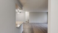 This single-story, 2-bedroom, 2-bathroom residence offers a thoughtfully designed layout that makes efficient use of its space. The open-concept living and kitchen area serves as the heart of the home, featuring rich, dark hardwood-style flooring throughout. The kitchen is equipped with stainless steel appliances, including a range, microwave, and refrigerator, complemented by white cabinetry, a tile backsplash, granite countertops, and a peninsula with a built-in sink — ideal for both cooking and casual dining. Track lighting illuminates the kitchen, while a ceiling fan adds comfort to the living area. A sliding glass door floods the living room with natural light and provides exterior access. Both bedrooms are finished with soft carpeting and neutral-toned walls. The primary bedroom is a comfortable size and includes a walk-in closet and direct access to a bathroom. The second bedroom features a large window that brings in ample natural light. The bathrooms are clean and functional, featuring granite-topped vanities with white cabinetry and tub/shower combinations. A dedicated in-unit laundry area with wire shelving adds everyday convenience. The home's consistent neutral palette and modern finishes create a clean, cohesive aesthetic throughout.