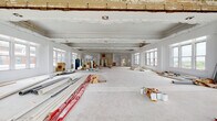 This single-floor space is a historically significant property currently in the midst of an active renovation. The building's architectural character is immediately evident through its elaborate, hand-crafted plaster moldings and ornamental detailing that run along the ceilings and upper walls throughout multiple rooms. These intricate decorative elements — including scrollwork, floral relief panels, and classical cornicing — speak to the building's heritage and craftsmanship.

The layout spans several generously proportioned, open rooms connected by wide doorways. Ceilings are notably high, lending an impressive sense of volume and grandeur to each area. Large, multi-pane windows line the exterior walls in nearly every room, flooding the interiors with natural light and framing views of the surrounding urban and natural landscape.

One area features a distinctive curved or rotunda-style alcove, adorned with an ornate carved plaster wall panel, adding further architectural interest. Structural columns are present in certain zones, contributing to the overall form of the space.

The floors are currently exposed concrete or bare subfloor throughout, awaiting finishes. While construction materials, scaffolding, and renovation supplies are presently visible, they reflect an ongoing transformation. This space presents a compelling opportunity to restore and repurpose a richly detailed historic interior with substantial square footage and outstanding natural light.