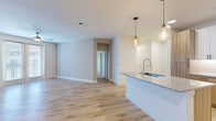 This single-floor residence showcases a thoughtfully designed open-concept layout that seamlessly connects the kitchen and living areas. The kitchen is outfitted with two-tone cabinetry — combining warm wood lower cabinets with crisp white upper cabinets — complemented by granite countertops, a stainless steel sink, and a full suite of stainless steel appliances including a refrigerator, range, and over-the-range microwave. A kitchen island with pendant lighting serves as both a functional workspace and a visual centerpiece.

The open living area features light wood-look flooring, neutral-toned walls, and a ceiling fan, with natural light streaming in through a set of French doors. A dedicated hallway leads to the private quarters, including bedrooms finished with plush carpeting, ceiling fans, and windows with blinds that allow for comfortable natural light.

The bathroom is finished with light wood-look flooring, white vanity cabinetry with matte black hardware, a rectangular mirror, and a tiled tub-shower combination. The consistent use of neutral tones, modern fixtures, and quality materials throughout creates a clean, cohesive aesthetic that is both functional and inviting.