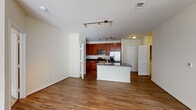 This single-floor residence offers a thoughtfully designed open-concept layout that seamlessly connects the kitchen, dining, and living areas. The kitchen is a functional centerpiece, featuring rich cherry wood cabinetry, dark granite countertops, a suite of stainless steel appliances including a gas range, microwave, and French door refrigerator, and a central island with a built-in sink — ideal for both cooking and casual dining. Track lighting overhead provides ample illumination throughout the kitchen and main living area, which is finished with warm hardwood-style flooring that extends across the open floor plan. The living area is generously proportioned, with large windows that invite abundant natural light and lend an airy, open feel to the space. A dedicated pantry provides additional storage off the kitchen. The bedroom is carpeted for comfort, features a ceiling fan with light fixture, and is served by natural light through a sizable window. The bathrooms are finished with tile flooring, dark granite vanity tops, warm wood cabinetry, and a tiled shower-tub combination. A walk-in closet and in-unit laundry connections add further practicality. Clean neutral tones throughout create a cohesive and inviting atmosphere.