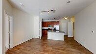 This single-floor residence offers a thoughtfully designed open-concept layout that seamlessly connects the kitchen, dining, and living areas. The kitchen is a functional centerpiece, featuring rich cherry wood cabinetry, dark granite countertops, a suite of stainless steel appliances including a gas range, microwave, and French door refrigerator, and a central island with a built-in sink — ideal for both cooking and casual dining. Track lighting overhead provides ample illumination throughout the kitchen and main living area, which is finished with warm hardwood-style flooring that extends across the open floor plan. The living area is generously proportioned, with large windows that invite abundant natural light and lend an airy, open feel to the space. A dedicated pantry provides additional storage off the kitchen. The bedroom is carpeted for comfort, features a ceiling fan with light fixture, and is served by natural light through a sizable window. The bathrooms are finished with tile flooring, dark granite vanity tops, warm wood cabinetry, and a tiled shower-tub combination. A walk-in closet and in-unit laundry connections add further practicality. Clean neutral tones throughout create a cohesive and inviting atmosphere.