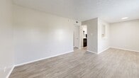 This single-story, 2-bedroom, 1-bathroom unit offers a thoughtfully organized layout designed for comfortable everyday living. Throughout the space, light wood-look luxury vinyl flooring creates a clean, cohesive aesthetic that ties every room together. The living room serves as the heart of the home, featuring a classic fireplace with a white surround, two windows that allow natural light to fill the space, and direct access to the front entry. An open passageway connects the living area to the kitchen, which is visible in the background and equipped with standard appliances. Both bedrooms are well-proportioned, each featuring textured ceilings, neutral wall tones, and dedicated closet space — one bedroom includes a sliding-door closet with a full rod, while the primary bedroom benefits from a walk-in closet. Each bedroom also features a window, providing natural light and ventilation. The bathroom is clean and functional, offering a single-sink vanity with white cabinetry, a quartz-style countertop, brushed nickel fixtures, and a large mirror. Recessed lighting and flush-mount ceiling fixtures provide consistent illumination throughout. The overall aesthetic is neutral, bright, and move-in ready, making efficient use of every square foot available.