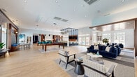 Located at 8130 Prescott Dr in Vienna, VA, this generously sized single-floor community clubhouse offers a thoughtfully designed interior that blends modern aesthetics with functional gathering spaces. Light wood-look tile flooring flows throughout, unifying the open-plan layout beneath high ceilings fitted with recessed lighting and contemporary pendant fixtures.

The main social area is anchored by a full-size billiards table and surrounded by comfortable lounge seating in rich navy and neutral tones, with large windows drawing in abundant natural light and views of the outdoor pool. A café-style bar area features counter seating, warm wood cabinetry, and a bold aviation-themed accent wall that adds a striking visual focal point.

A dedicated lounge nook with high-back chairs and built-in shelving provides a quieter retreat, while a separate dining and meeting room — enclosed by glass partitions — offers a more formal setting with a large wood conference table, an accent TV wall, and direct pool views through oversized windows. Additional seating areas with communal tables, pendant lighting, and geometric accent walls serve as flexible co-working or social spaces. The entry corridor features curated large-scale artwork, and multiple access points connect the interior seamlessly to the outdoor amenity areas.