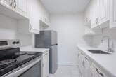 Located at 2202 Weston Rd in Toronto's Weston neighbourhood, this one-bedroom, one-bathroom unit offers a clean, modern aesthetic across a thoughtfully laid-out single floor. The open combined living and dining area is bright and airy, anchored by large windows that frame views of surrounding trees and flood the space with natural light. Light-toned laminate wood flooring runs throughout the main living areas and bedroom, lending warmth and continuity to the design. Recessed pot lights complement the natural light in the living area, enhancing the sense of openness.

The galley-style kitchen is efficiently designed with white cabinetry on both sides, white countertops, a stainless steel refrigerator, and a stove with oven — providing ample storage and workspace. Light ceramic tile flooring completes the kitchen's clean, functional look.

The bedroom is a comfortable, well-proportioned retreat featuring the same warm wood flooring, a large window overlooking the treetops, a radiator heating unit, and a built-in sliding-door closet offering generous storage. The bathroom is finished with bright white subway-style wall tiles surrounding a full soaker tub, paired with a pedestal-style sink for a classic, clean look. Overall, the unit presents a bright, neutral palette throughout.