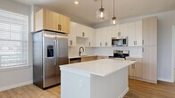 Located on Legendary Loop in Wesley Chapel, FL, this well-appointed single-story home offers three bedrooms, four bathrooms, and a thoughtfully designed layout. The open-concept kitchen and living area serves as the heart of the home, showcasing a large center island with a crisp white quartz countertop, two-tone cabinetry combining white upper cabinets with warm natural wood lower cabinets, a herringbone tile backsplash, stainless steel appliances, and globe pendant lighting over the island. Light wood-look flooring runs throughout the main living areas, adding warmth and continuity. The bedrooms feature plush carpeting and bright windows with views to the outdoors, while ceiling fans provide comfort. Three spacious closets, including a walk-in with wire shelving systems, offer generous storage. The four bathrooms are finished in a clean, modern style with light wood vanities, black hardware accents, and light wood-look flooring. Bathrooms include both tub/shower combos with marble-style tile surround and separate glass-enclosed walk-in showers. A stacked washer and dryer unit is conveniently integrated into the hallway area. The overall aesthetic is contemporary and cohesive, with neutral tones and quality finishes throughout.