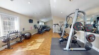 Located at 2726 Jacqueline Dr in Wilmington, Delaware, this single-floor fitness center is a well-appointed facility designed to support a full range of workout routines. The space features warm hardwood flooring throughout, complemented by neutral beige walls, recessed lighting, and vaulted ceilings that lend an open, airy feel. Natural light streams generously through multiple large windows fitted with white blinds, while a set of glass French doors with a transom window at one end provides additional brightness and a welcoming entry point.

The cardio zone is anchored by a row of Vision treadmills lined along one wall, alongside elliptical trainers and a stationary cycle, offering ample options for cardiovascular training. Wall-mounted televisions provide entertainment during workouts. The strength training area is equally comprehensive, featuring a Precor cable/weight machine, a Smith machine with bench, a multi-functional cable resistance unit, a dumbbell rack, weight plates, and a stability ball. Large wall mirrors in the strength zone enhance the sense of space and allow for proper form checks during exercise. Rubber floor mats protect the hardwood in high-use lifting areas. The overall layout is thoughtfully organized to separate cardio and strength zones, creating a functional, comfortable, and professional fitness environment.