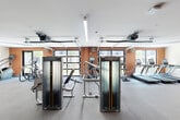 Located in Huntsville, Alabama, this fitness center offers a generously sized, single-floor exercise space designed to support a wide range of workout routines. The room features a modern, open layout with durable flooring throughout, providing ample space for movement between equipment stations.

The facility is outfitted with a robust selection of Matrix-brand strength machines, including cable systems and functional trainers, alongside a dedicated free weights area stocked with a full rack of dumbbells and kettlebells, medicine balls, and resistance accessories. Cardio equipment includes multiple treadmills and stair climbers, all positioned to take advantage of the natural light streaming in through large, garage-style glass doors that open toward outdoor views.

The warm orange accent walls contrast with the clean white ceiling, giving the space an energetic and motivating ambiance. Recessed and linear LED lighting ensures the interior remains bright throughout. A mirrored wall section enhances the sense of space and aids in form monitoring during workouts. The facility is accessed through double glass entry doors and includes clearly marked emergency exits, reflecting a strong attention to both functionality and safety throughout the design.