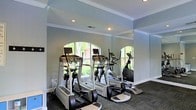 Located at 3300 Grove Crabtree Crescent in Raleigh, NC, this fitness center offers a well-equipped, single-floor workout space designed to support an active lifestyle. The room features a carefully curated selection of modern cardio equipment, including treadmills, ellipticals, and upright exercise bikes, all arranged for comfortable use and easy circulation. Large arched windows along one wall allow abundant natural light to fill the space, providing pleasant views of lush greenery outside. Full-length mirrors reflect both the natural light and the outdoor scenery, creating a sense of openness and making the room feel more expansive. The walls are finished in a soft, neutral tone that contributes to a calm and focused atmosphere, while crisp white crown molding and baseboards add a refined architectural detail. Recessed lighting supplements the natural light, ensuring the space remains bright and functional at any hour. Dark, low-pile carpeting covers the floor, providing traction and comfort underfoot during workouts. The overall ambiance is clean, welcoming, and purpose-built, offering residents a convenient and comfortable environment to maintain their fitness routines.