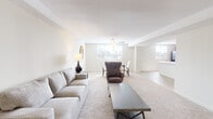 This single-floor residence offers a thoughtfully designed layout that balances open communal spaces with comfortable private quarters. The living area is generously proportioned, featuring neutral carpet, white walls, and multiple windows that allow natural light to fill the room. A ceiling fan overhead adds both function and a subtle design element. The space flows naturally into a dedicated dining area, creating a cohesive and versatile entertaining environment.

The kitchen is anchored by a large curved peninsula with a light countertop and an integrated sink, providing abundant workspace and casual seating potential. Dark-stained cabinetry lines the walls, offering substantial storage, while black appliances — including a refrigerator, range, and over-the-range microwave — complete the functional setup. Wood-look flooring grounds the kitchen area distinctly from the adjoining spaces.

The bedrooms are carpeted and well-lit, each equipped with ceiling fans and windows overlooking outdoor greenery. The primary bedroom includes a spacious walk-in closet with wire shelving. Bathrooms feature tile flooring, and one includes a full tub-shower combination with white tile surround. A separate half bath provides added convenience for guests.