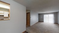 This single-floor unit is designed with a practical, straightforward layout that maximizes usable space across its rooms. Neutral gray walls and warm wood-toned baseboards create a consistent aesthetic throughout, lending the space a clean, understated character. Textured popcorn ceilings are present in the main living and bedroom areas, while hard-surface wood-look flooring runs through the kitchen and bathroom.

The galley-style kitchen is efficiently organized, featuring white cabinetry with wood-trim accents along both walls, white appliances including a refrigerator and electric range, a black dishwasher, and a double-basin sink with ample counter space. A hard-surface floor adds durability to this high-traffic area.

The main living area is generously proportioned, with plush carpeting and a sliding glass door fitted with vertical blinds that allows natural light to filter in. An open pass-through cutout connects the living space to an adjacent area, adding visual depth. A separate dining or secondary living zone features hard-surface flooring and a ceiling light fixture.

The bedrooms are carpeted and well-lit, each equipped with windows fitted with blinds that bring in natural light. The full bathroom includes a soaking tub with shower, a vanity with mirror, wood-accented cabinetry, and hard-surface flooring.