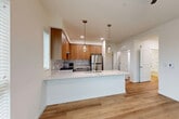 Located at Metro 319 in Lynnwood, Washington, this single-floor residence showcases a clean, contemporary design highlighted by warm light wood flooring that flows seamlessly throughout the entire space. The open-concept kitchen serves as the centerpiece of the home, featuring a large peninsula with a white quartz countertop, an undermount sink, and stylish pendant lighting with Edison-style bulbs. Cabinetry is thoughtfully designed with a two-tone combination of warm wood-tone upper cabinets and sleek gray lower cabinets, complemented by a soft gray subway tile backsplash. Stainless steel appliances — including a refrigerator, range, built-in microwave, and range hood — complete the well-appointed kitchen. Natural light filters in through multiple windows, brightening the bedroom spaces, which offer ceiling fans and a clean, neutral palette. The bathroom is well-equipped with a full soaking tub and shower combination featuring built-in shelving, along with a separate vanity area boasting white countertops, gray cabinetry, a large mirror, and an adjacent walk-in closet with wire shelving. The overall ambiance is bright, modern, and move-in ready, reflecting thoughtful design and quality finishes throughout.