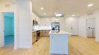 Located at 2553 Brentwood Dr in Clearwater, Florida, this single-story home showcases a thoughtfully designed interior with a cohesive modern aesthetic. Light wood-tone flooring runs continuously throughout the space, complementing the bright white walls and creating a warm, airy atmosphere.

The kitchen serves as the centerpiece of the open-concept living area, featuring a two-tone cabinet design that pairs crisp white upper cabinetry with natural wood-finish lower cabinets, all accented by matte black hardware. A large central island with a white countertop and an undermount sink with a black faucet provides ample workspace and casual seating. Stainless steel appliances, including a refrigerator, range, and microwave, are integrated seamlessly. Pendant lighting above the island and recessed ceiling lights complete the space. The open layout connects the kitchen directly to the living area, which includes a ceiling fan and access to an in-unit laundry area.

The bedrooms are well-proportioned, featuring large windows that invite natural light and include closet access. The bathrooms carry the same design language, with wood-finish vanities, white countertops, black hardware, and tub-shower combinations.