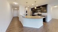 Located at 7525 Post Rd in North Kingstown, Rhode Island, this thoughtfully designed single-floor residence offers a clean, contemporary living experience. The open-concept main area seamlessly connects the living space to the kitchen, where rich dark cabinetry contrasts beautifully with a curved granite-topped island. Pendant lighting illuminates the island, complementing the recessed ceiling lights throughout. Stainless steel appliances, including a refrigerator, microwave, and range, complete the well-equipped kitchen. A stacked in-unit washer and dryer provides added convenience. Hardwood-style flooring flows throughout the main living areas, adding warmth and continuity, while crown molding lends an elegant finishing touch. Natural light pours in through multiple windows, including a set of large windows in the living area that offer views of the surrounding neighborhood, as well as a glass exterior door. The bedroom features plush carpeting and a bright window overlooking the outdoors. Two bathrooms are finished with classic black-and-white hexagonal tile flooring — one offering a soaking tub with shower combination, and the other a walk-in shower with a built-in bench. The result is a fresh, move-in-ready space that balances style and function.