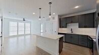This well-appointed two-bedroom, two-bathroom single-floor residence offers a thoughtfully designed open-concept layout. The kitchen and living area flow seamlessly together, anchored by a central island with a crisp white countertop and illuminated by a pair of stylish globe pendant lights. The kitchen is outfitted with gray flat-front cabinetry, stainless steel appliances, a white subway tile backsplash, and a matte black faucet over an undermount sink. Light hardwood-style flooring extends throughout the main living areas, complemented by recessed lighting and a ceiling fan.

Both bedrooms are carpeted and feature ceiling fans, large windows with horizontal blinds that invite ample natural light, and generous proportions. The primary bedroom connects directly to an en-suite bathroom, which showcases large-format tile flooring, marble-look tile in the walk-in shower, dark gray cabinetry with a white quartz vanity, and matte black hardware throughout. Each bedroom is served by a dedicated closet, with the primary closet offering built-in shelving and hanging rods. The second bathroom mirrors the refined aesthetic of the primary. The overall design palette of whites, grays, and natural wood tones creates a clean, contemporary ambiance throughout.
