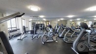 This fitness center offers a practical and well-organized space for residents or members to pursue their health and wellness goals. The room is outfitted with a solid selection of cardio equipment, including multiple treadmills and a stationary recumbent bike, positioned to allow comfortable spacing between machines. A dedicated strength training area features a cable/pull-up tower and a dumbbell rack, providing options for a full-body workout without the need to leave the facility.

Large mirrors line the walls, visually expanding the space and allowing users to monitor their form during exercise. The dark rubber flooring provides durability and cushioning underfoot, making it well-suited for high-impact activity. Overhead flush-mount lighting ensures the room is consistently and evenly illuminated throughout.

A textured ceiling adds a classic finish to the space, while a window along one wall introduces a degree of natural light and a connection to the outdoors. The overall layout is efficient and uncluttered, offering a clean and functional environment that accommodates both cardio and strength training needs within a single, cohesive space.