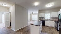 Located at 8251 Ranchview Dr in Irving, Texas, this single-story residence offers a thoughtfully designed, open-concept layout that seamlessly connects the kitchen and living areas. The kitchen is a standout feature, equipped with white cabinetry, a stone-look tile backsplash, dark granite-style countertops, and a suite of black appliances including a refrigerator, range, microwave, and dishwasher. A central island provides additional prep space and serves as a natural dividing point between the kitchen and the adjoining living room. Rich wood-look flooring runs throughout the main living and kitchen areas, lending warmth and cohesion to the space. The living room benefits from natural light streaming through multiple windows and is fitted with a ceiling fan for year-round comfort. The bedrooms are carpeted and well-sized, each featuring windows that invite natural light and walk-in closets with built-in shelving for ample storage. The primary bathroom is a practical retreat, outfitted with a dual-sink vanity, a large framed mirror, stylish vanity lighting, dark countertops, and a full tub-shower combination with white tile surround. Wood-look flooring continues in the bathroom areas, maintaining a consistent aesthetic throughout the home.