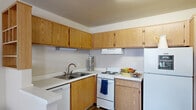 This well-organized one-bedroom, one-bathroom unit offers a practical and functional layout across a single floor. The open-concept design connects the kitchen, dining, and living areas into one cohesive space, maximizing the efficient use of the floor plan.

The kitchen is equipped with an L-shaped arrangement of warm oak cabinetry extending to the ceiling for ample storage. It includes white appliances — a refrigerator, electric range with overhead ventilation, and dishwasher — as well as light-toned countertops and a stainless steel sink. Wood-look flooring runs throughout the kitchen and living areas, lending a clean, cohesive appearance.

The living room provides a comfortable gathering space with a window that brings in natural light, a wall-mounted AC unit, and a front entry door. A small dining area with room for a compact table sits just off the kitchen.

The bedroom features wall-to-wall carpeting, a window with natural light, a wall-mounted AC unit, and direct access to a dedicated walk-in closet — offering practical storage solutions. The textured ceiling is consistent throughout the unit.

The bathroom includes a full tub-shower combination with tile surround, a toilet, and a vanity mirror, providing all essential amenities in a compact, functional layout.
