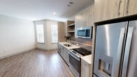 This 500 square foot studio apartment in Herndon, VA offers a thoughtfully designed living space that maximizes functionality and style. The heart of the home is the modern kitchen, boasting light wood-toned cabinetry that extends to the ceiling, providing ample storage. Stainless steel appliances, including a built-in microwave and electric range, complement the sleek design. A striking grey subway tile backsplash adds visual interest, while quartz countertops offer durability and elegance.

The bathroom continues the contemporary aesthetic with a floating vanity, large mirror, and modern fixtures. In-unit laundry facilities are conveniently tucked away. The main living area features wood-look vinyl flooring that unifies the space and adds warmth. Large windows allow natural light to flood the room, creating an airy ambiance. Recessed lighting throughout ensures proper illumination at all hours.

The open floor plan encourages a seamless flow between living, dining, and sleeping areas, making the space feel larger than its 500 square feet. Clean lines and a neutral color palette provide a canvas for personal style. This efficient studio combines modern amenities with smart design, offering a comfortable urban living experience.