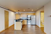 Located at 314 N Franklin St in downtown Madison, WI, this one-bedroom, two-bathroom unit offers a well-designed layout that maximizes every square foot. The open-concept kitchen and living area serves as the heart of the space, featuring light maple cabinetry, dark granite-style countertops, a peninsula with pendant lighting, and a full suite of stainless steel appliances including a refrigerator, electric range, microwave, and dishwasher. Recessed lighting and warm-toned hardwood-style flooring create a bright, inviting atmosphere in the main living area. Large windows with views of the surrounding neighborhood allow natural light to fill the space throughout the day. The bedroom is a quiet, carpeted retreat with a double-door closet and a dedicated window that brings in additional natural light. Two bathrooms serve the unit, each finished with maple vanities, dark countertops, and tile flooring, maintaining a consistent design language with the rest of the space. A hallway connects the rooms efficiently, contributing to a clean and functional flow. The unit's compact yet thoughtfully organized footprint makes it a practical option for urban living in the heart of Madison.