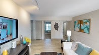 This single-floor residence presents a thoughtfully designed layout with a consistent teal, gray, and warm neutral color scheme carried throughout. The living room is a welcoming gathering space featuring wood-look flooring, track lighting overhead, and direct sightlines to the bedrooms, creating an open and connected feel. A dedicated dining area showcases a bold teal accent wall, a large round pendant light, mirrored wall panels, and a glass-top dining table, adding a stylish, intimate atmosphere to the space.

The kitchen is well-equipped with taupe shaker-style cabinetry, granite-patterned countertops, a tile backsplash, and a full suite of stainless steel appliances including a refrigerator, dishwasher, microwave, and electric range. Multiple bedrooms offer plush carpeting, natural light through large windows with drapery, and ample room for furnishings. The bathroom includes a tub-shower combination, wood-look flooring, a vanity with storage, and a lighted mirror. Throughout the residence, neutral wall tones and consistent finishes create a cohesive, move-in-ready environment.