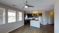 This single-floor residence offers a thoughtfully designed open-concept layout that seamlessly connects the living and kitchen areas, creating a spacious and inviting atmosphere. The kitchen is a standout feature, showcasing dark espresso cabinetry that contrasts elegantly with light countertops, including a generously sized center island that serves as both a prep space and a casual gathering point. Stainless steel appliances — including a refrigerator, range, microwave, and dishwasher — add a sleek, contemporary touch. Pendant lighting and a track light fixture illuminate the kitchen, enhancing both function and ambiance. The living area benefits from abundant natural light streaming through multiple windows fitted with horizontal blinds, and a ceiling fan with an integrated light fixture adds comfort and airflow to the space. Rich, dark hardwood-style flooring runs throughout, tying the open layout together with warmth and visual continuity. Neutral gray walls provide a clean, versatile backdrop that complements the modern design palette. The textured ceiling adds subtle dimension, while clean white baseboards frame each room with a crisp finish. Overall, this residence delivers a modern, functional, and well-appointed living environment.
