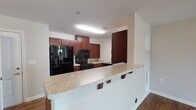 This single-story unit in Spotsylvania, Virginia, offers a practical and cohesive layout designed for comfortable everyday living. Wood-look flooring runs consistently throughout the main living areas, bedrooms, and bathroom, providing a warm, unified aesthetic across the space.

The kitchen is a functional centerpiece, equipped with rich cherry wood cabinetry offering generous storage, light-toned countertops with subtle veining, and a full suite of black appliances including a side-by-side refrigerator with an in-door ice and water dispenser and a gas range. A raised breakfast bar extends from the kitchen into the adjoining living area, creating a natural division between the two spaces while offering casual seating. The open connection between the kitchen and living room enhances the overall sense of space and flow.

The living area is generously sized, featuring neutral-toned walls and a ceiling-mounted light fixture. An adjacent room, suitable as a bedroom, includes a ceiling fan with integrated lighting and a paneled closet door for storage.

The bathroom is clean and well-appointed, featuring a vanity with a marble-style countertop, a wide mirror, cherry cabinetry below, and a full-size tub and shower combination. Wood-look flooring continues here, complementing the overall design. The space is practical, with grab bars installed near the toilet and tub for added accessibility.