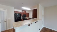 This single-story unit in Spotsylvania, Virginia, offers a practical and cohesive layout designed for comfortable everyday living. Wood-look flooring runs consistently throughout the main living areas, bedrooms, and bathroom, providing a warm, unified aesthetic across the space.

The kitchen is a functional centerpiece, equipped with rich cherry wood cabinetry offering generous storage, light-toned countertops with subtle veining, and a full suite of black appliances including a side-by-side refrigerator with an in-door ice and water dispenser and a gas range. A raised breakfast bar extends from the kitchen into the adjoining living area, creating a natural division between the two spaces while offering casual seating. The open connection between the kitchen and living room enhances the overall sense of space and flow.

The living area is generously sized, featuring neutral-toned walls and a ceiling-mounted light fixture. An adjacent room, suitable as a bedroom, includes a ceiling fan with integrated lighting and a paneled closet door for storage.

The bathroom is clean and well-appointed, featuring a vanity with a marble-style countertop, a wide mirror, cherry cabinetry below, and a full-size tub and shower combination. Wood-look flooring continues here, complementing the overall design. The space is practical, with grab bars installed near the toilet and tub for added accessibility.