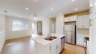 This well-designed two-story residence offers a clean, contemporary aesthetic throughout, characterized by neutral tones, light-toned luxury vinyl plank flooring on the main level, and plush carpeting in the upper-floor bedrooms. The open-concept kitchen serves as a central hub of the main floor, showcasing white shaker-style cabinetry reaching to the ceiling, a center island with a double-basin sink and light countertops, and a full suite of stainless steel appliances including a refrigerator, range, microwave, and dishwasher. The adjacent living area is bright and airy, benefiting from natural light through large windows and a glass-paneled door leading to an outdoor balcony, complemented by a ceiling fan overhead. Carpeted stairs connect the floors, leading to the upper level where the bedrooms feature soft carpet, ceiling fans, and windows with blinds that allow for natural light and privacy. The primary bathroom offers an elongated vanity with undermount sink, white cabinetry, and access to a walk-in closet. The attached garage provides generous enclosed parking with an automatic opener. Throughout the home, recessed lighting, white panel doors, and a cohesive neutral palette create a clean, move-in-ready environment.