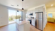 Located at 630 N Kelly Ave in Oklahoma City, this thoughtfully designed two-bedroom, two-bathroom residence offers a clean, modern aesthetic throughout. Light wood-tone flooring flows consistently across the single level, complementing the bright white walls and creating a cohesive, airy feel.

The open-concept kitchen serves as the heart of the home, anchored by a large center island with an undermount sink and light quartz countertops. White flat-front cabinetry, stainless steel appliances — including a refrigerator, range, and microwave — and stylish pendant lighting complete the space. A full-length sliding glass door opens to a private balcony, filling the living area with natural light and offering pleasant treetop views.

Both bedrooms are well-proportioned and bright, with large windows that bring in ample sunlight and views of the surrounding neighborhood. Each room features light wood flooring and direct access to closet storage. The primary bedroom includes a dedicated closet and convenient proximity to the kitchen area.

The two bathrooms are finished in a neutral palette. One features a tub-shower combination with white tile surround and brushed hardware, while the other includes a vanity with under-sink storage and wood-tone flooring. The overall design emphasizes clean lines, functional layouts, and a bright, welcoming ambiance throughout.