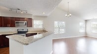 Located at 711 Superior Ct in Naperville, IL, this well-appointed single-floor home offers three bedrooms and two full bathrooms across a efficiently designed floor plan. The open-concept kitchen is a standout feature, showcasing rich dark cabinetry, granite countertops, stainless steel appliances including a range, microwave, and refrigerator, and a peninsula with a built-in sink that opens toward the living area. The living and dining area is bathed in natural light from multiple windows fitted with blinds, and features warm hardwood flooring, vaulted ceilings, a ceiling fan, and sliding glass door access to a private outdoor deck. The spacious primary bedroom continues the hardwood flooring and offers a sliding glass door with outdoor views. The two additional bedrooms are carpeted and finished with neutral tones, providing versatile spaces for various needs. Both bathrooms feature white-tiled tub and shower combinations with chrome fixtures and clean, bright finishes. Textured ceilings and consistent neutral wall tones throughout lend the home a cohesive, move-in-ready aesthetic. A hallway and dedicated closet complete the practical layout of this comfortable Naperville residence.