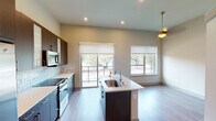 Located at 1025 Preston Rd in Plano, Texas, this single-floor space offers a thoughtfully designed modern interior with clean lines and contemporary finishes throughout. The kitchen is a standout feature, equipped with a full suite of stainless steel GE appliances including a side-by-side refrigerator with ice maker, a range, and an over-the-range microwave. Dark espresso cabinetry with sleek hardware contrasts beautifully against white quartz countertops and a textured tile backsplash. A central island with an undermount sink provides additional workspace and casual seating potential. Light wood-look flooring runs throughout the open-plan living and dining areas, which are bathed in natural light from a sliding glass door leading to an outdoor balcony and multiple windows with views of mature trees. The elevated ceilings enhance the sense of openness, while recessed lighting and a decorative pendant fixture add warmth. The bathroom features a dark-framed vanity mirror, undermount sink, and quartz countertop, maintaining the home's cohesive modern aesthetic. An additional room with a ceiling fan and wood-look flooring offers flexible use as a bedroom or office space.