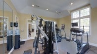 Located at 8800 Cattail Creek Pl in Raleigh, NC, this single-floor fitness center is thoughtfully designed to provide a comprehensive workout environment. The space is bathed in natural light through multiple windows, creating a bright and energizing atmosphere that complements the warm, neutral-toned walls and recessed lighting overhead.

The fitness area is well-equipped with a professional multi-station cable and weight machine as its centerpiece, offering a wide range of strength training exercises. Alongside it, cardio equipment including a stair climber and additional machines are strategically positioned to maximize the use of the space. Non-slip diamond-plate flooring panels are placed beneath the equipment for added safety and durability.

The layout is open and spacious, allowing for comfortable movement between stations. Large windows on multiple walls invite the outdoors in, offering pleasant views of the surrounding greenery while working out. French doors connect the fitness area to an adjacent room, adding to the sense of openness and accessibility throughout the facility.

With its clean design, quality equipment, and abundance of natural light, this fitness center offers a practical and motivating environment well-suited for a variety of exercise routines.