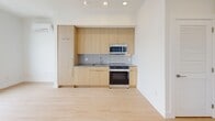 Unit 506 at 1440 N Front St is a thoughtfully designed one-bedroom, one-bathroom residence located on the fifth floor in Philadelphia's vibrant Fishtown neighborhood. Light wood-tone flooring runs throughout the unit, creating a warm and cohesive aesthetic that ties each room together seamlessly.

The open kitchen anchors one end of the living space, outfitted with flat-front light wood cabinetry that extends floor to ceiling for generous storage. Gray subway tile backsplash, dark countertops, a stainless steel sink, and stainless steel appliances — including an electric range and over-the-range microwave — complete the clean, modern look.

The bedroom is a bright and airy retreat, featuring large grid-pane windows that frame sweeping views of the Philadelphia cityscape. A wall-mounted ductless HVAC unit ensures year-round comfort. The room benefits from abundant natural light and a dedicated closet for ample storage.

The bathroom is finished with floor-to-ceiling vertical subway tile in a warm taupe tone, complemented by neutral stone-look floor tile. A full soaking tub with an overhead shower, a built-in niche, and brushed nickel fixtures round out the well-appointed space.

The unit also includes a dedicated entrance area, adding a practical buffer between the hallway and living space. Clean lines, a neutral palette, and modern finishes give this unit a polished, move-in-ready appeal.