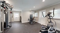 Located in Atlanta's 30316 zip code, this dedicated exercise room offers a well-designed, functional fitness space ideal for a comprehensive workout routine. The room is finished with a neutral gray palette on the walls, accented by clean white trim, crown molding, and shiplap-style wall detailing that lends a polished, modern aesthetic throughout.

The durable speckled rubber flooring provides excellent traction and impact absorption, making it well-suited for a variety of exercise activities. Recessed ceiling lighting ensures the space is brightly and evenly illuminated, while multiple windows fitted with white blinds allow for natural light and ventilation.

A wall-mounted mini-split HVAC unit provides dedicated climate control, ensuring comfort during any season. The space accommodates a range of professional-grade equipment, including a Matrix treadmill, a Matrix elliptical trainer, a cable crossover strength training machine, and a selectorized weight bench — offering options for both cardiovascular and resistance training.

Multiple entry points, including two exterior doors, provide convenient access. The thoughtful layout leaves sufficient open floor space for stretching or additional equipment. Overall, this exercise room delivers a private, climate-controlled, and fully functional fitness environment.