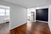 This 2-bedroom, 1-bathroom unit at 939E Western Rd in London, Ontario, offers a efficiently organized single-floor layout finished with rich, dark hardwood-style flooring that runs consistently throughout the main living areas and bedrooms, providing a cohesive and clean aesthetic.

The living room is an open, rectangular space with white walls, including a distinctive dark accent wall that adds visual contrast. It connects directly to the kitchen, which features white cabinetry, stainless steel appliances including a refrigerator and range, light tile flooring, and a window with a radiator unit beneath it for heating.

The primary bedroom is a well-proportioned room benefiting from natural light through a wide set of windows fitted with blinds, a textured ceiling, and a radiator heater. The second bedroom is a quieter, more compact space with warm neutral walls, hardwood-style flooring, and a sliding-door closet offering organized storage with a shelf and hanging rod.

The bathroom is finished in light tile and features a pedestal sink, toilet, wall-mounted storage cabinet, and a vanity mirror. A hallway connects the rooms, providing a practical and straightforward circulation path throughout the unit.