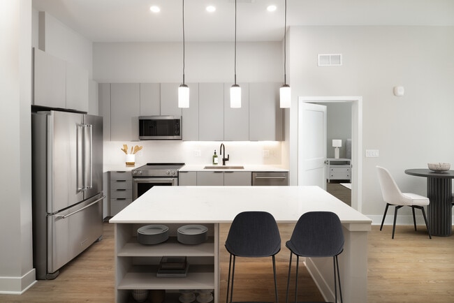 Cocina Signature Collection con electrodomésticos de acero inoxidable, gabinetes de color gris claro, encimeras y protector contra salpicaduras de cuarzo marmolado, iluminación debajo de los gabinetes, estantes empotrados y pisos de superficie dura. - Avalon at Becker Farm
