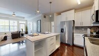 Located on Colton Court in St. Charles, Illinois, this single-floor residence offers a thoughtfully designed open layout that integrates the kitchen, dining, and living areas into a cohesive, functional space. Rich dark hardwood flooring anchors the main living and kitchen areas, creating a striking contrast against the white cabinetry and neutral wall tones throughout.

The kitchen is a standout feature, equipped with crisp white shaker-style cabinetry extending to the ceiling, a mosaic tile backsplash, granite countertops, and a full suite of stainless steel appliances. A central island with open shelving and pendant lighting above serves as both a prep space and a casual dining bar with seating.

The living room features a tray ceiling with a ceiling fan, abundant natural light from multiple windows, and a sleek built-in linear fireplace framed by a classic white surround—an elegant focal point for the room. A half-wall with a bar-height ledge visually separates the kitchen from the living space while maintaining an open feel.

The bedrooms are carpeted for comfort, bathed in natural light from large windows with neighborhood views, and include walk-in closets with built-in shelving. The overall ambiance is clean, modern, and welcoming throughout.