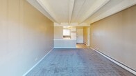 This single-floor unit offers a practical, open layout defined by a spacious carpeted living area beneath a textured ceiling with distinctive exposed beams. The living space flows naturally toward a kitchen pass-through counter, which features wainscoting paneling along its base, providing a visual boundary while maintaining an open connection between the two areas. Baseboard heating runs along the perimeter walls, ensuring consistent warmth throughout.

The kitchen is well-equipped with white cabinetry, dark countertops, a tile floor, a full-size refrigerator, a gas range, and a built-in microwave. Track lighting illuminates the workspace, and a window above the sink allows natural light to brighten the area. Ample upper and lower cabinet storage adds functionality to the compact yet efficient layout.

The bedroom is generously sized, featuring the same exposed beam ceiling and carpeted flooring found in the living area. A sliding glass door opens directly to a private balcony, offering outdoor views and additional natural light.

The bathroom is clean and straightforward, with a tiled tub-and-shower combination, a window providing natural ventilation, and baseboard heating for comfort. The overall ambiance of the unit is understated and functional.