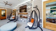 Located at 125 River Birch Grove Rd. in Asheville, NC, this single-level outdoor amenity space at Hawthorne at River Birch combines crafted architectural details with resort-style comfort. The exterior entrance is framed by stacked-stone columns, lap siding, and a warm wood-and-glass door, setting an inviting tone from the moment of arrival.

The centerpiece of the covered outdoor lounge is a dramatic floor-to-ceiling stacked-stone accent wall housing a linear gas fireplace topped with a rustic wood mantel, complemented by a wall-mounted television — ideal for year-round outdoor entertaining. Overhead, ceiling fans ensure comfortable airflow throughout the covered space.

The lounge area is furnished with hanging egg chairs and plush seating accented with bold orange throw pillows, all arranged over a patterned area rug. The space flows seamlessly to an open-air poolside terrace, where additional seating and dining options offer direct views of the swimming pool and surrounding lush greenery. Stone columns and black metal railings frame the terrace, reinforcing the cohesive design language throughout.

The interior fitness center, visible through the entrance door, completes the amenity suite. Together, these spaces deliver a well-appointed, community-focused environment that balances refined design with functional outdoor living in the heart of Asheville.