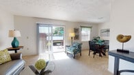 This single-floor residence offers a thoughtfully laid-out living space with a warm and inviting ambiance throughout. The living room serves as the heart of the home, featuring plush carpeting, a textured ceiling, and a large sliding glass door dressed with vertical blinds that opens to an outdoor patio — flooding the room with natural light and providing direct access to the exterior. A dedicated dining area sits adjacent, creating a seamless flow ideal for everyday living and entertaining.

The galley-style kitchen is efficiently designed with warm wood cabinetry lining both sides, laminate countertops, and white appliances including a range and refrigerator. A pass-through view connects the kitchen directly to the dining area, enhancing the open feel of the space.

The bedrooms are carpeted and tranquil, each offering ample room and natural light through well-positioned windows with classic curtains. The primary bedroom features soft, neutral tones and direct access to additional storage.

The bathroom is clean and functional, complete with a wide vanity, under-sink cabinetry, a wall mirror, and a shower-tub combination enclosed by a curtain. Throughout the home, neutral color palettes, soft carpet flooring, and consistent finishes contribute to a cohesive, comfortable living environment.